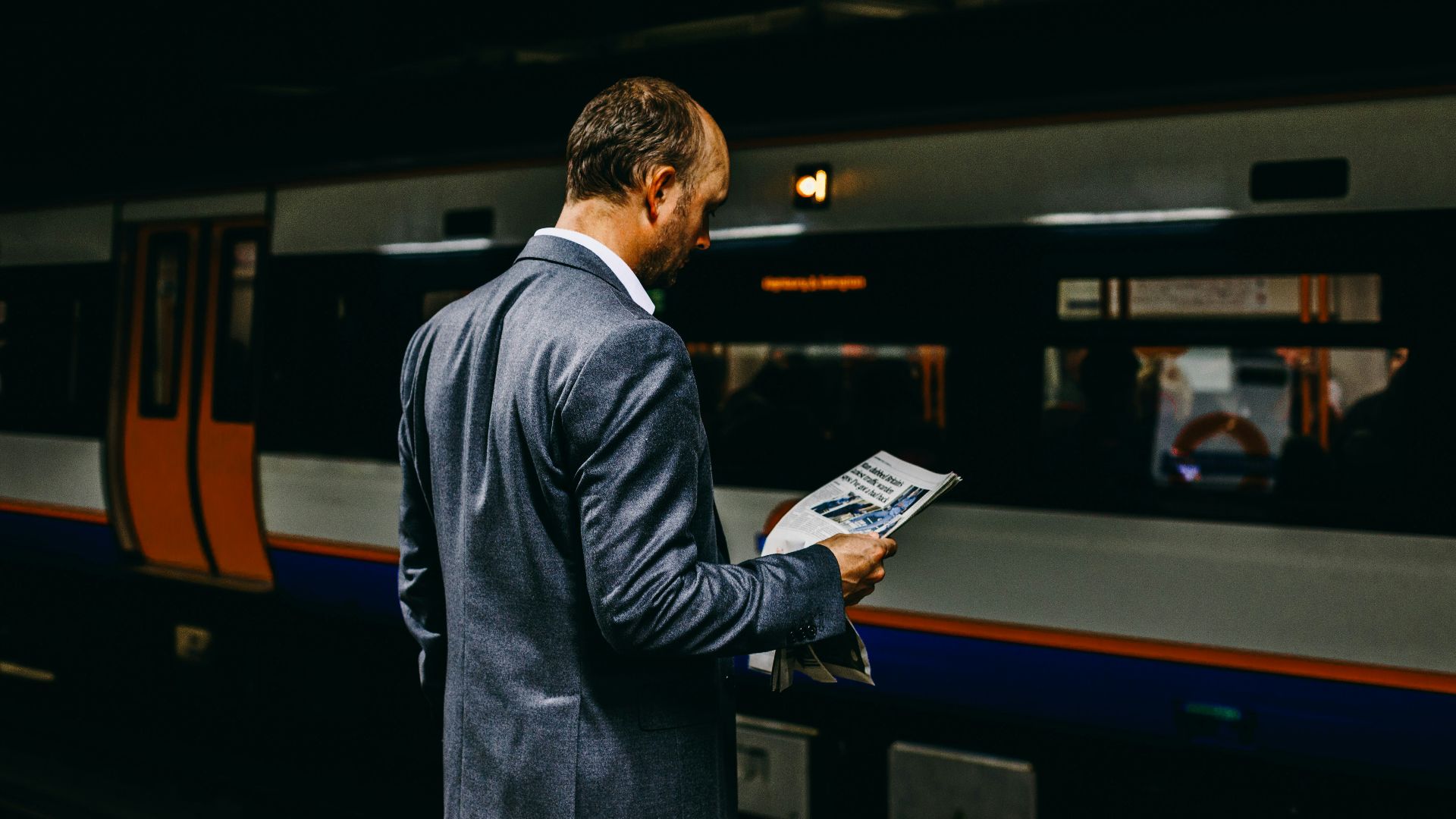 man holding newspaper standing on train station