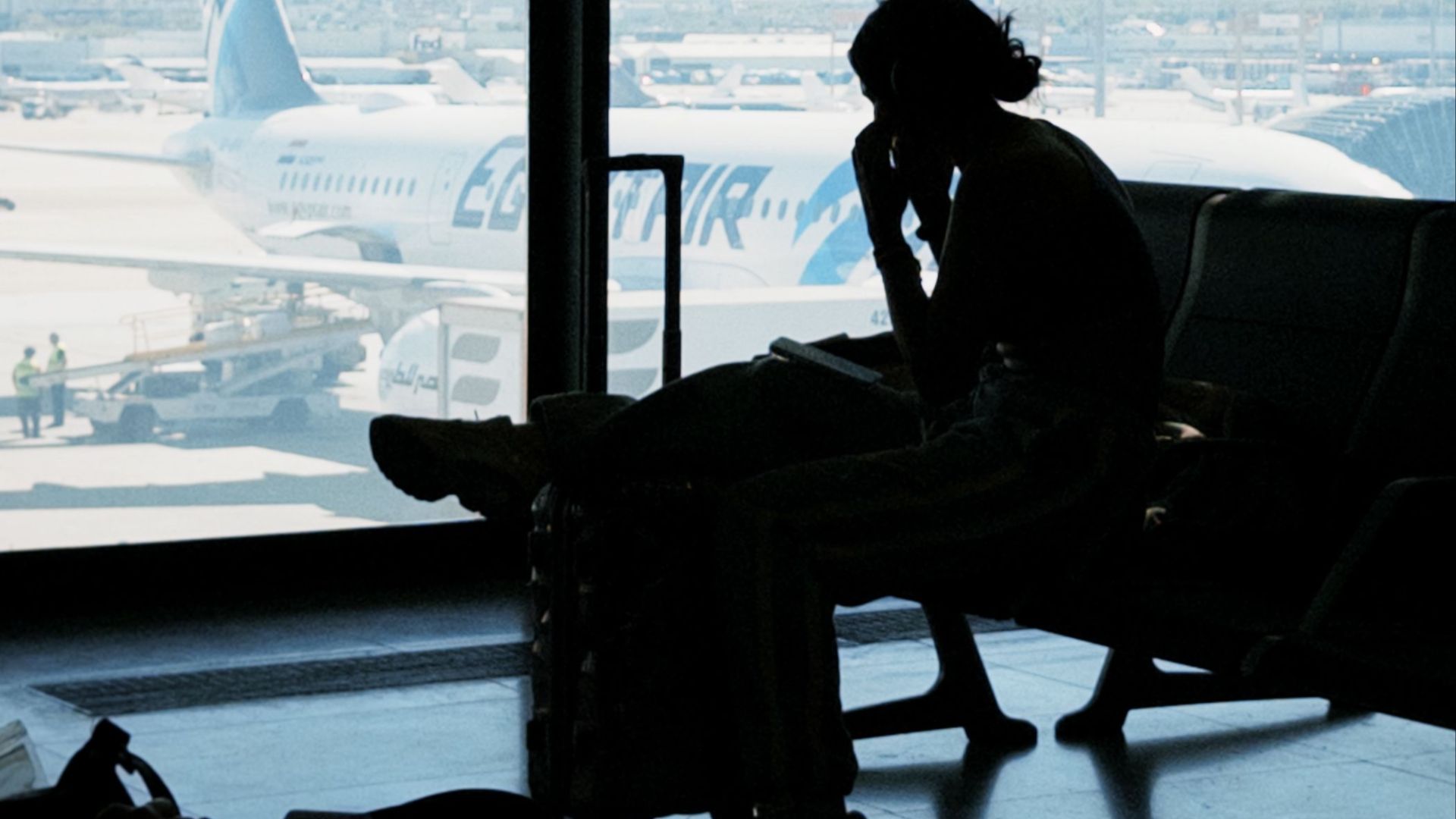 Silhouette of a person at an airport window with airplane view, embodying travel anticipation and solitude.