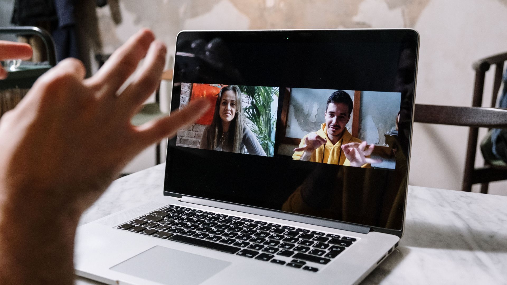 Hands gesturing during a video call on a laptop screen, showing two people in a virtual meeting.