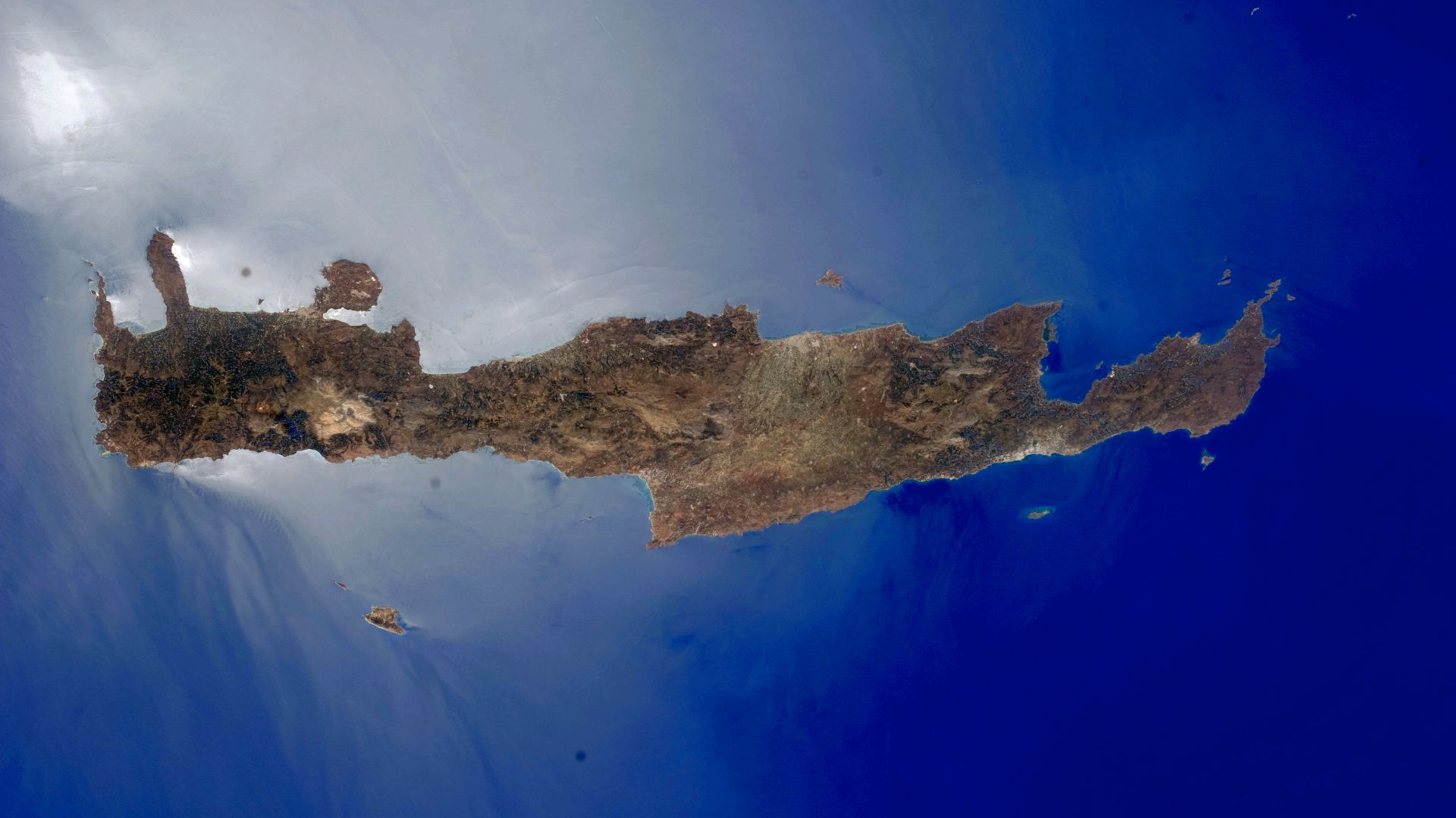 The western and central parts of Crete appear surrounded by quicksilver in this astronaut photograph taken from the International Space Station. This phenomenon is known as sunglint, caused by light reflecting off of the sea surface directly toward the ob