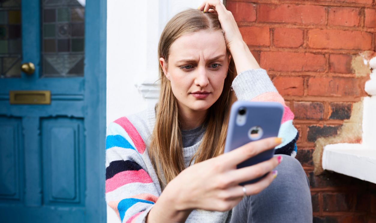 Young woman sitting outside a building, focused on her phone.