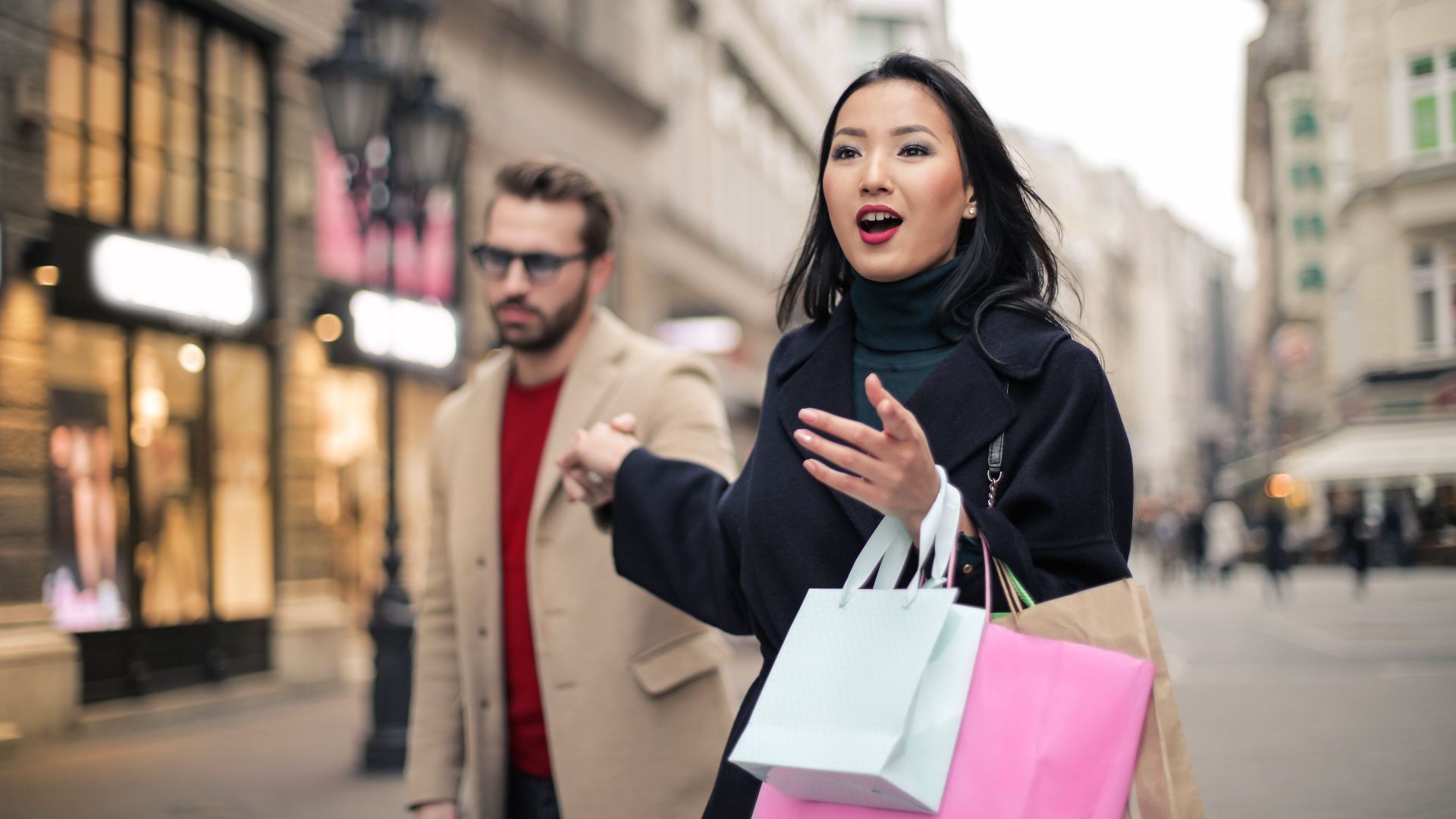 A couple enjoying a shopping day in a bustling city street, carrying colorful bags.