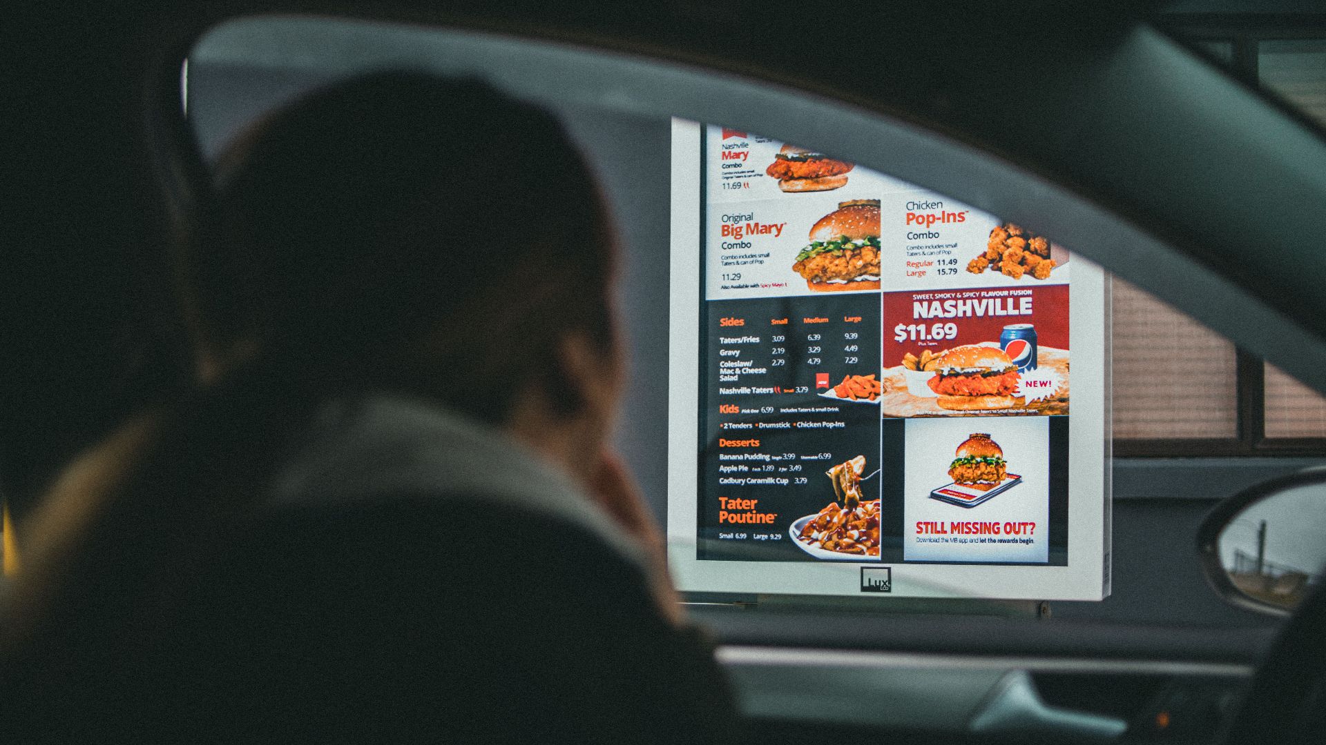 A woman in a car views the menu at a fast food drive-thru, ready to order her meal.