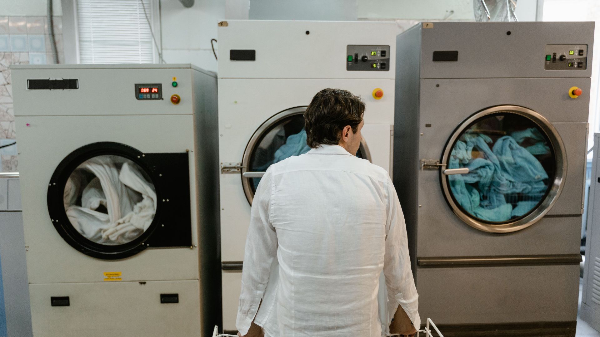 A man uses commercial washing machines at an indoor laundromat.