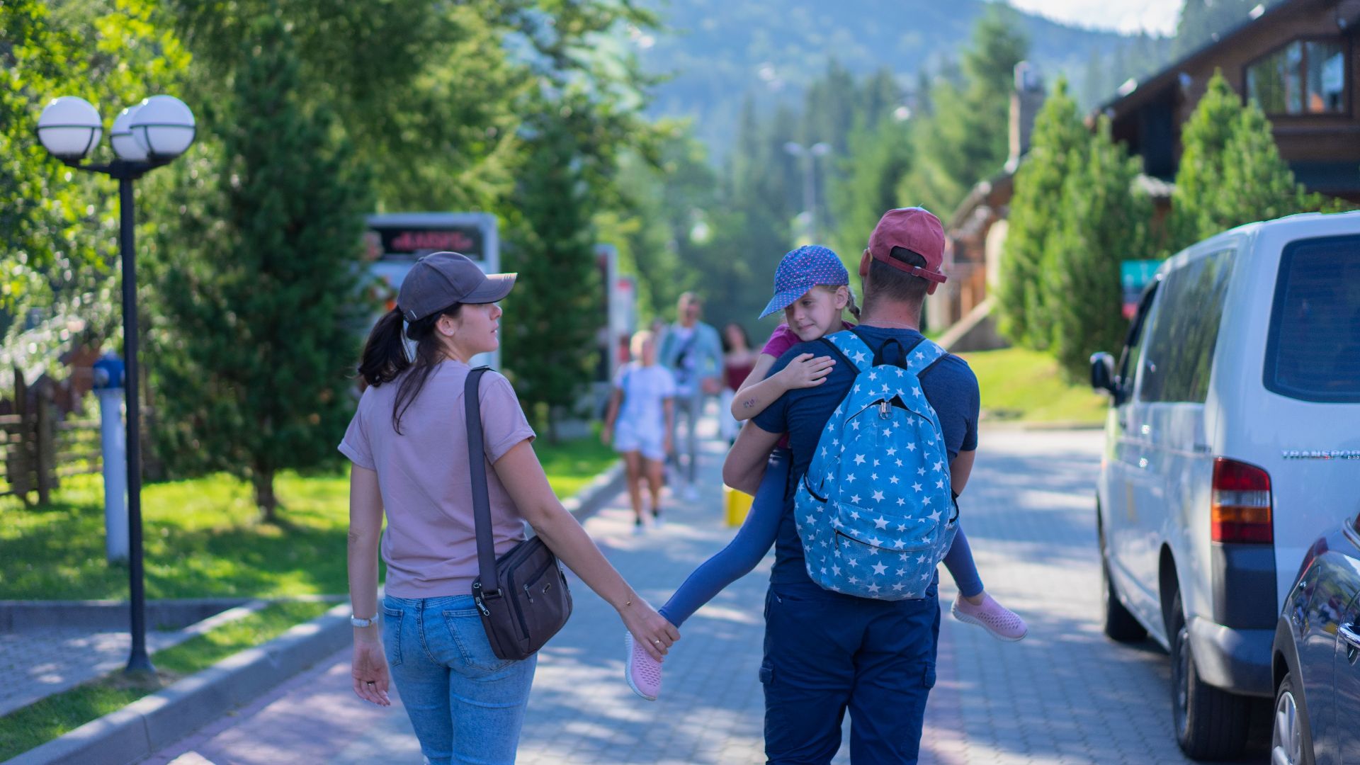 Parents walking with their daughter in a picturesque mountain village, enjoying a sunny day outdoors.