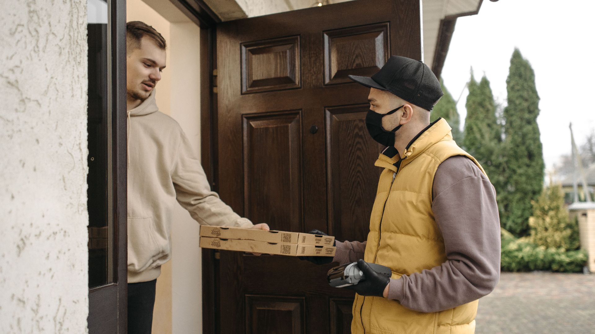 Courier delivering pizza boxes at the doorstep using contactless payment method.
