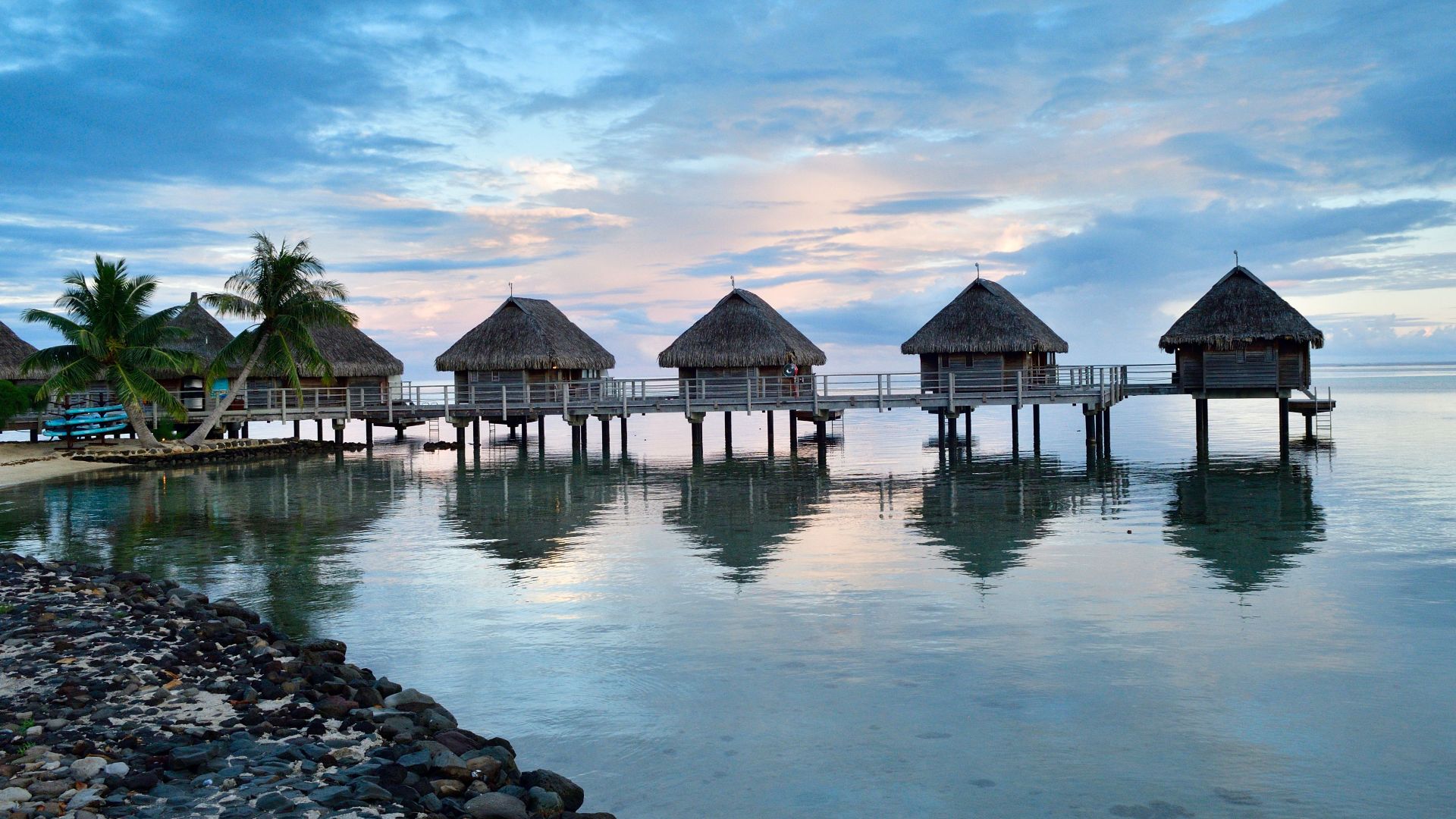 Picturesque overwater bungalows in Moorea, French Polynesia at sunset, reflecting in calm waters.