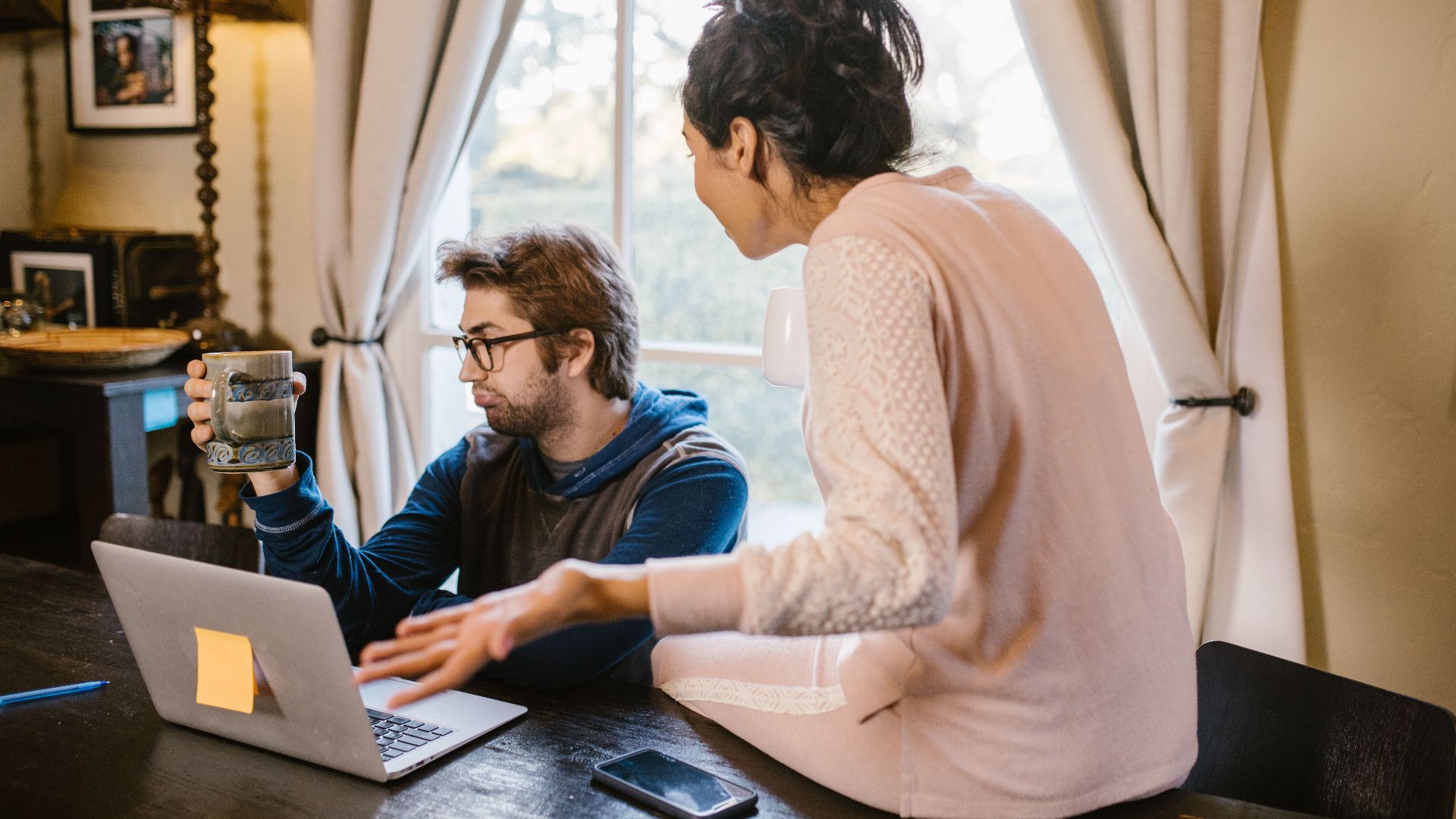 A couple engaged in a heated discussion indoors with a laptop open on the table.