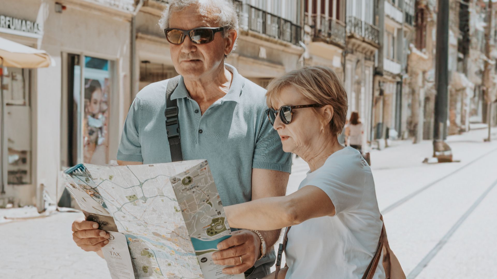 Senior couple in summer attire navigates with a map on a sunny Porto street.