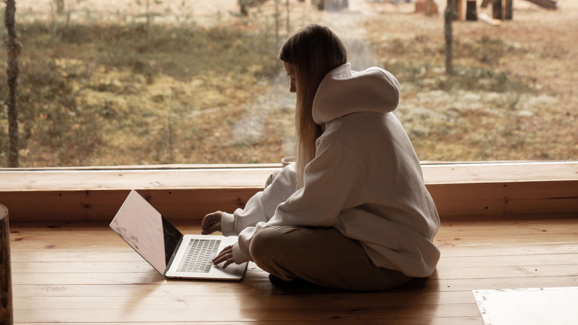 Woman working remotely in a cozy wooden cabin overlooking a serene lakeside view.