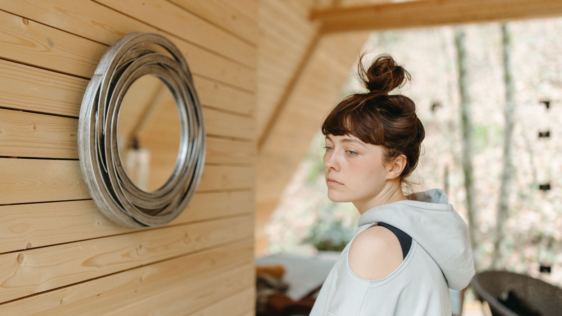 Woman in a hoodie with a bun stands indoors, embracing a cozy atmosphere.