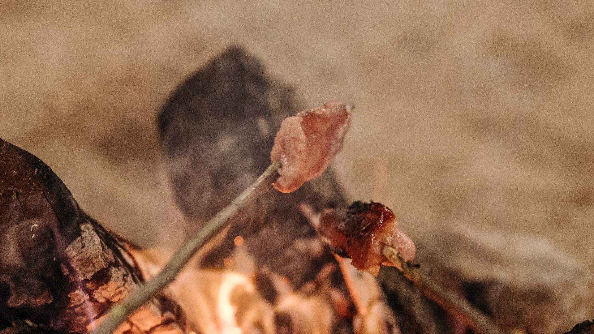 Skewered beef cooking on a campfire with crackling flames and smoke, capturing rustic outdoor culinary experience.