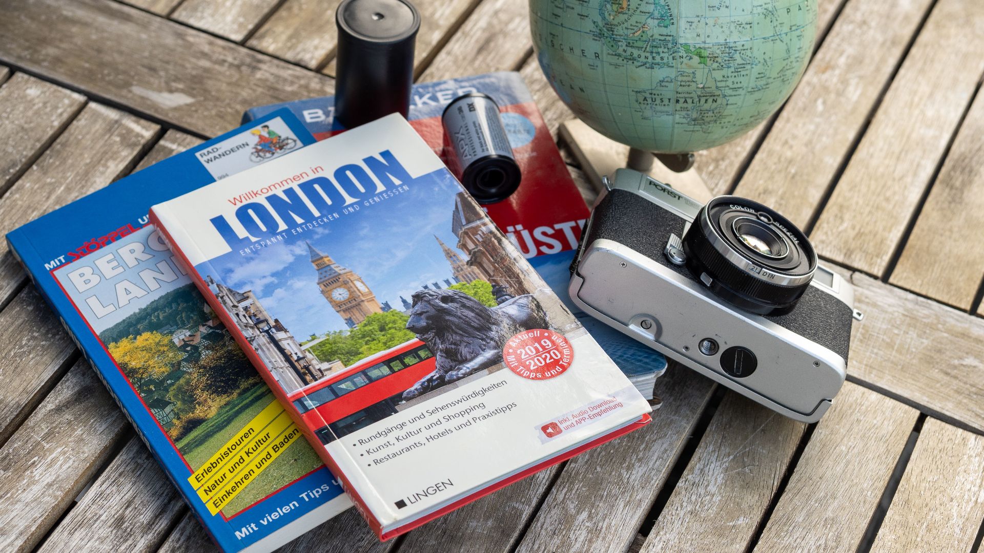 A vintage travel setup with guidebooks, a globe, and a film camera on a wooden table.
