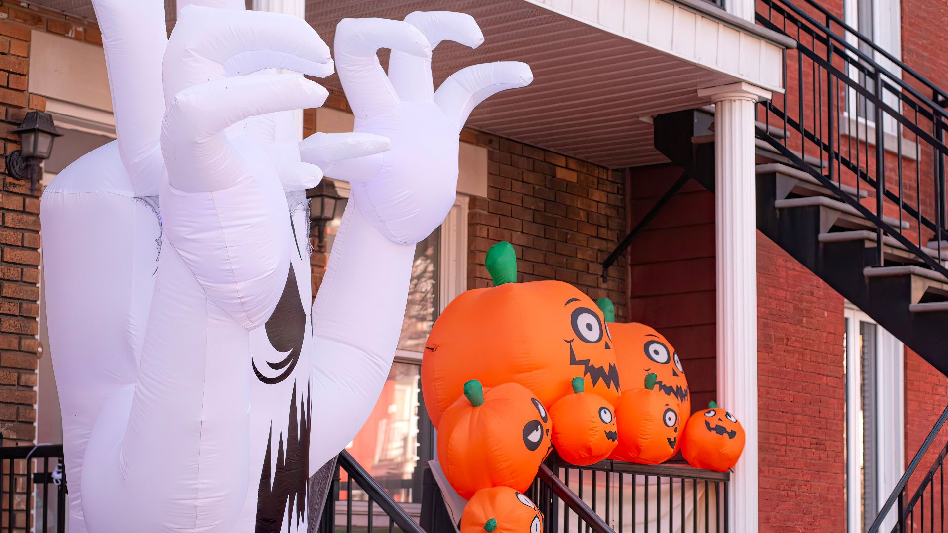 Inflatable ghost and pumpkins adorn a porch for Halloween in an urban setting.