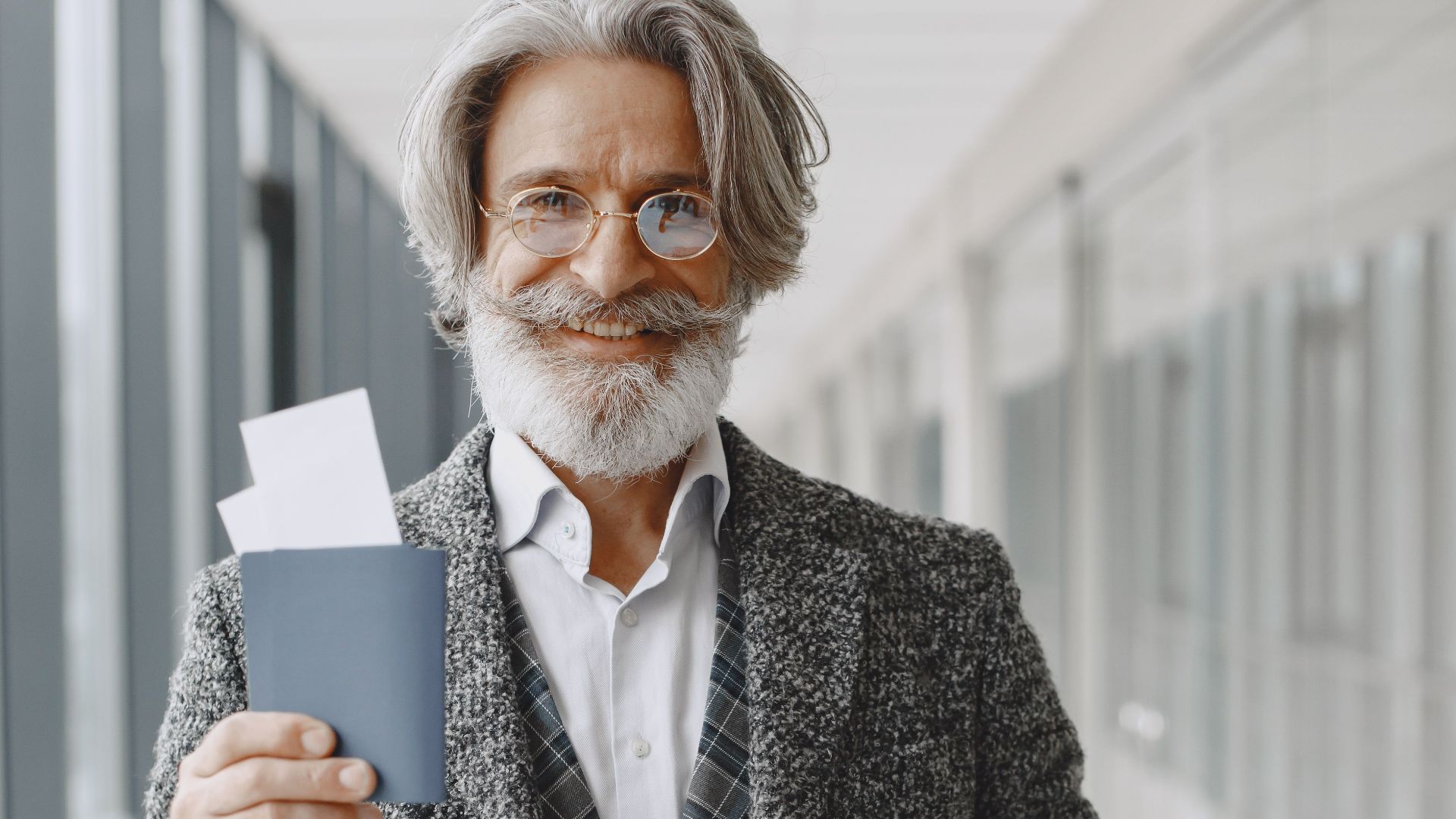 Elderly man in airport holding passport and luggage, smiling confidently at the camera.