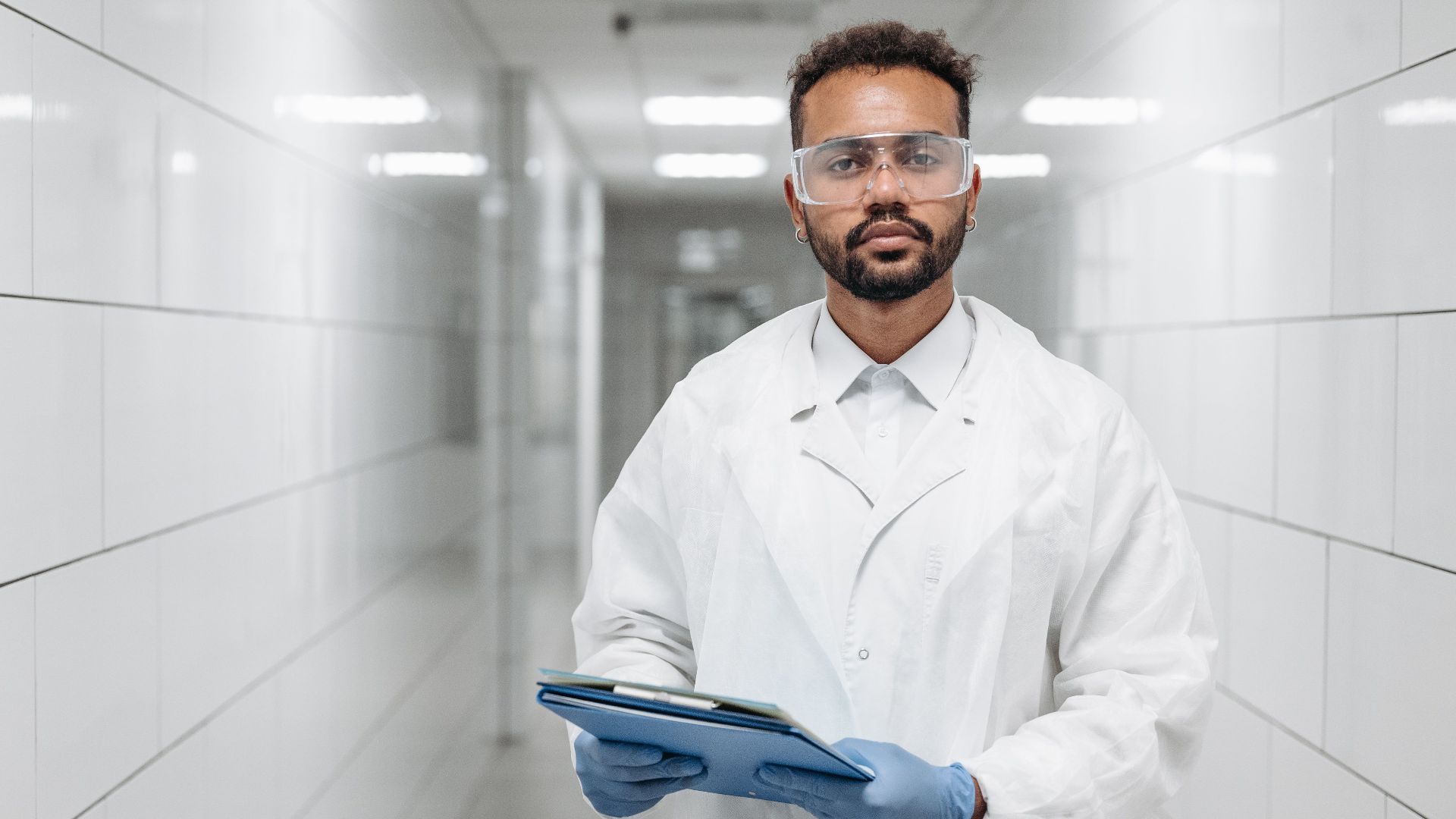 Portrait of a scientist in a laboratory hallway wearing protective goggles and gloves.