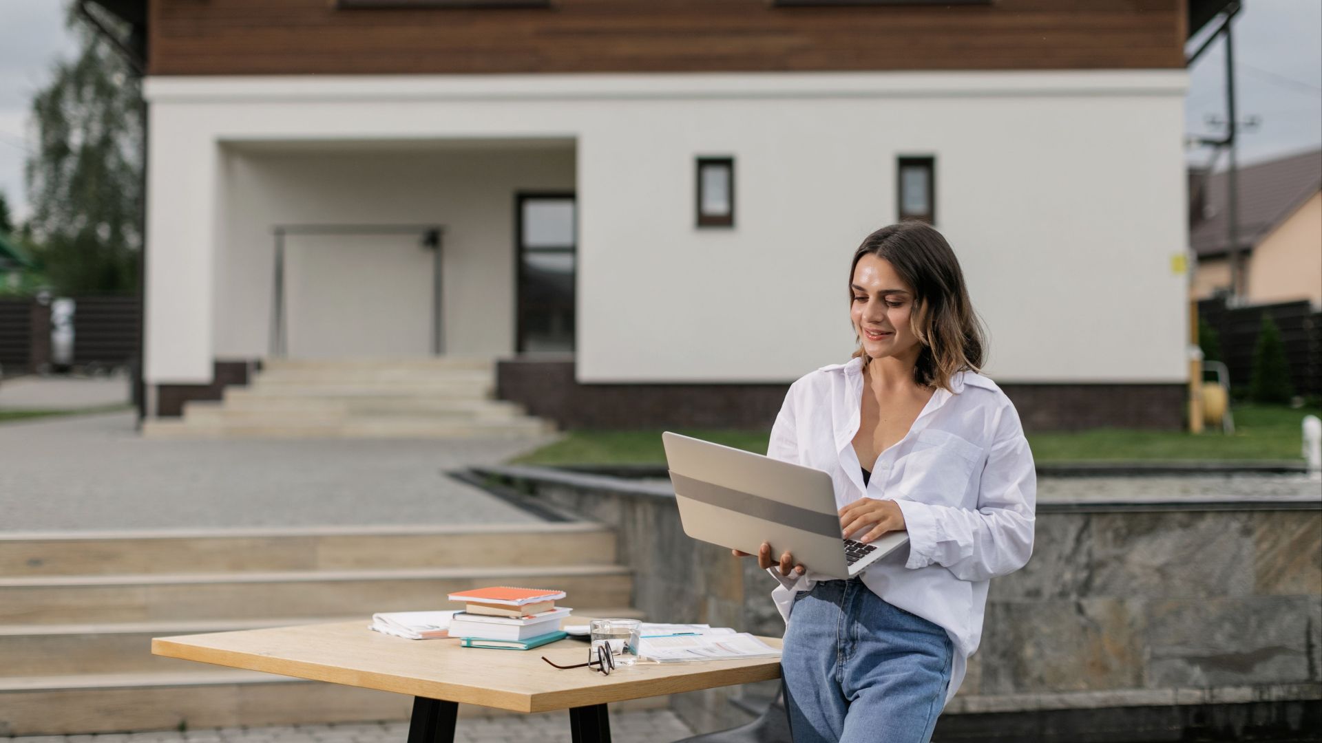 Woman in casual attire using a laptop outdoors at a table with books.