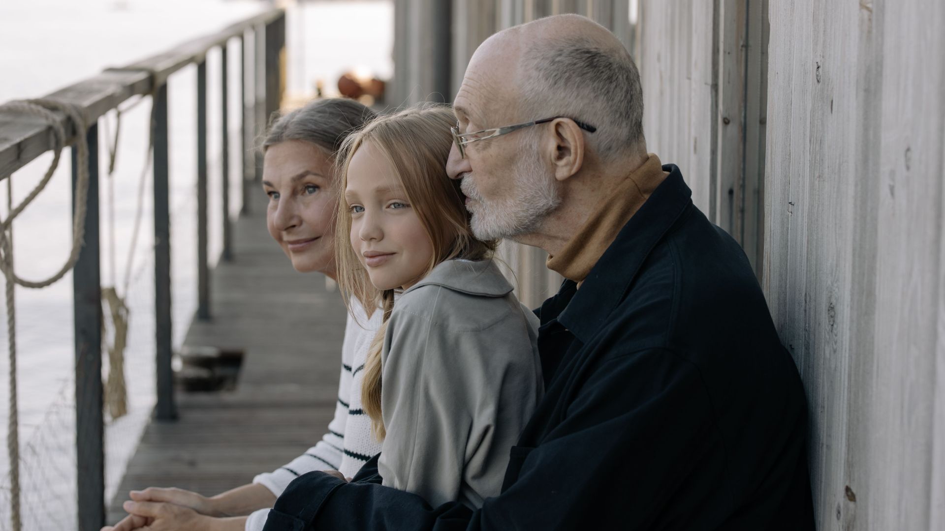 A loving family moment with grandparents and granddaughter sitting by the waterfront, outdoors.
