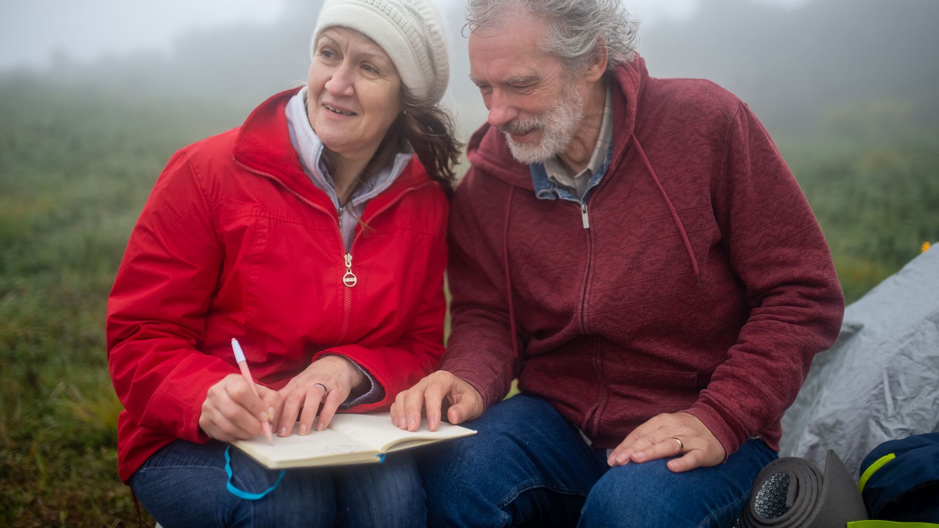 Elderly couple enjoys writing outdoors in misty Portugal landscape.