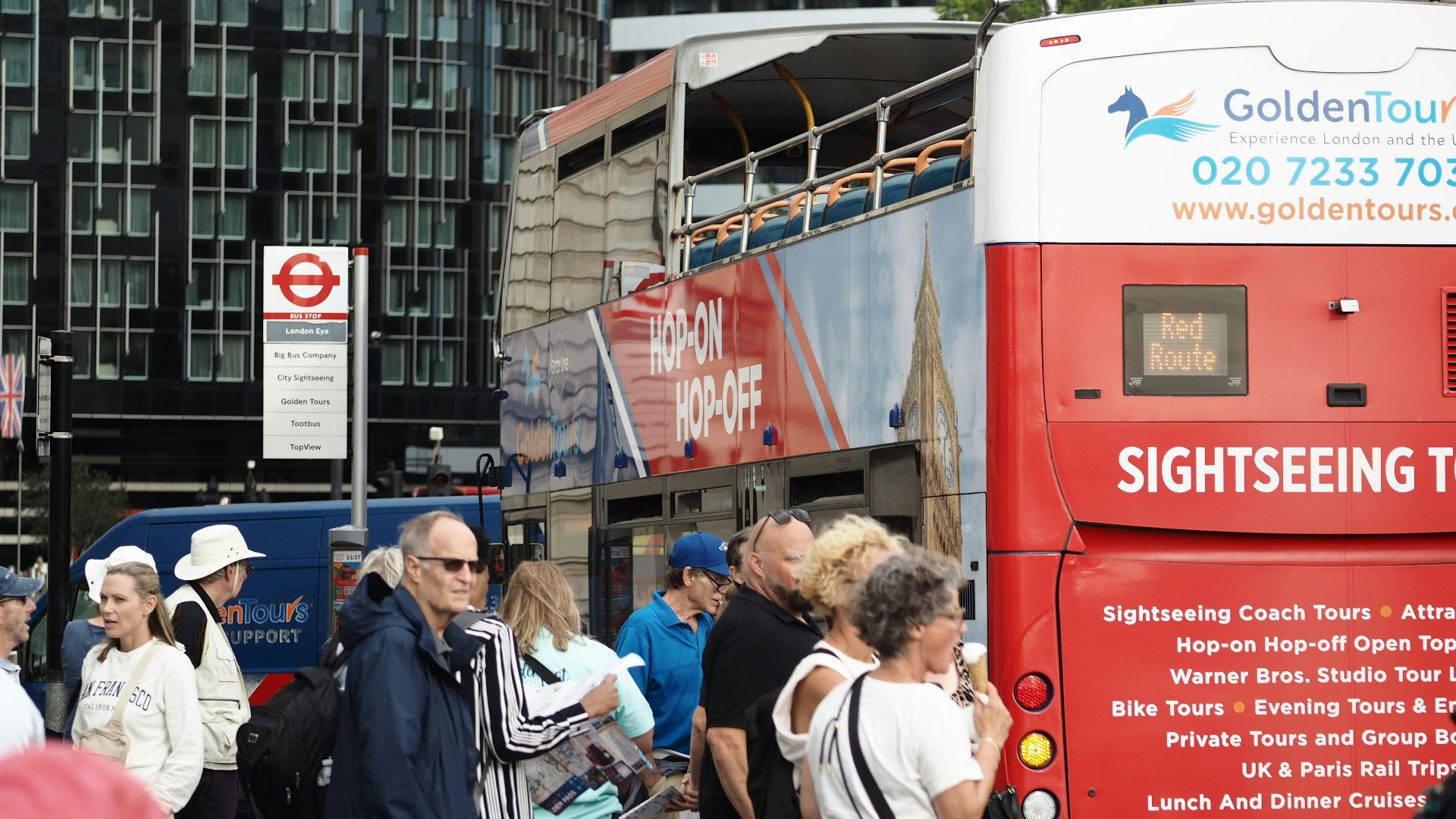 A group of tourists waiting for a red double-decker sightseeing bus in London