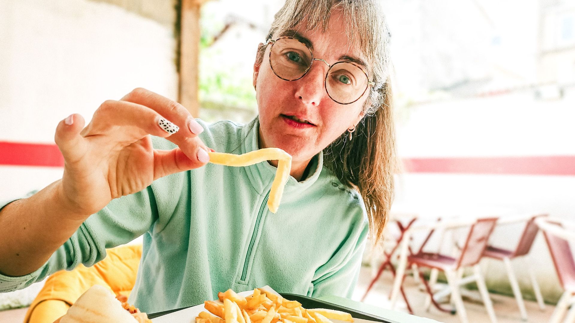 Woman with eyeglasses holding French fries at an outdoor cafe in Bergerac, France.