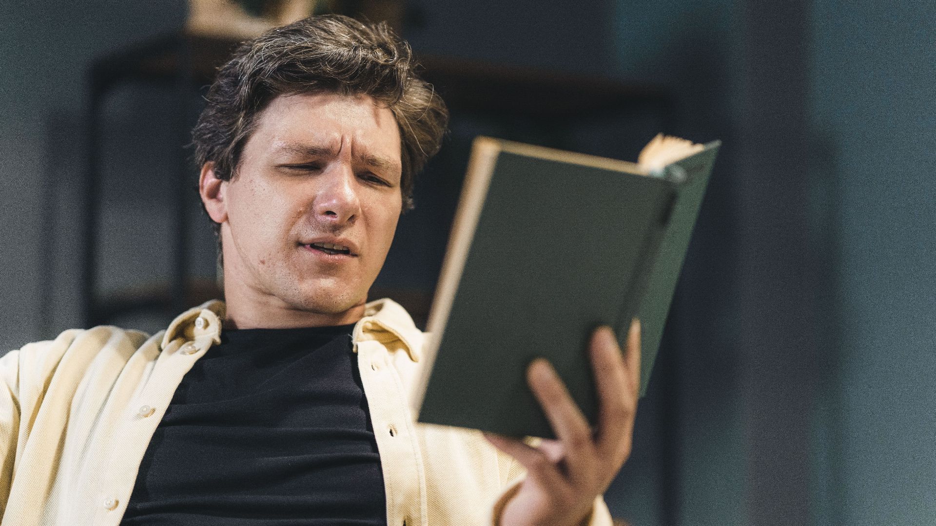 Man deeply engaged in reading a book, expressing curiosity or confusion.