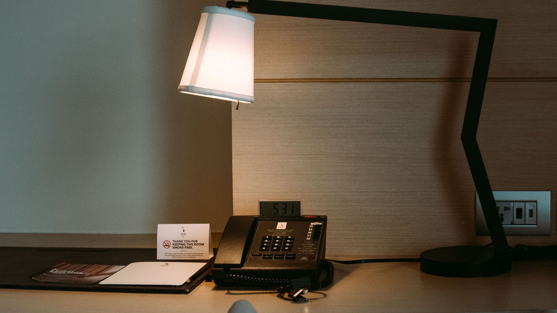 A modern hotel room desk featuring a stylish lamp, telephone, and stationery set.