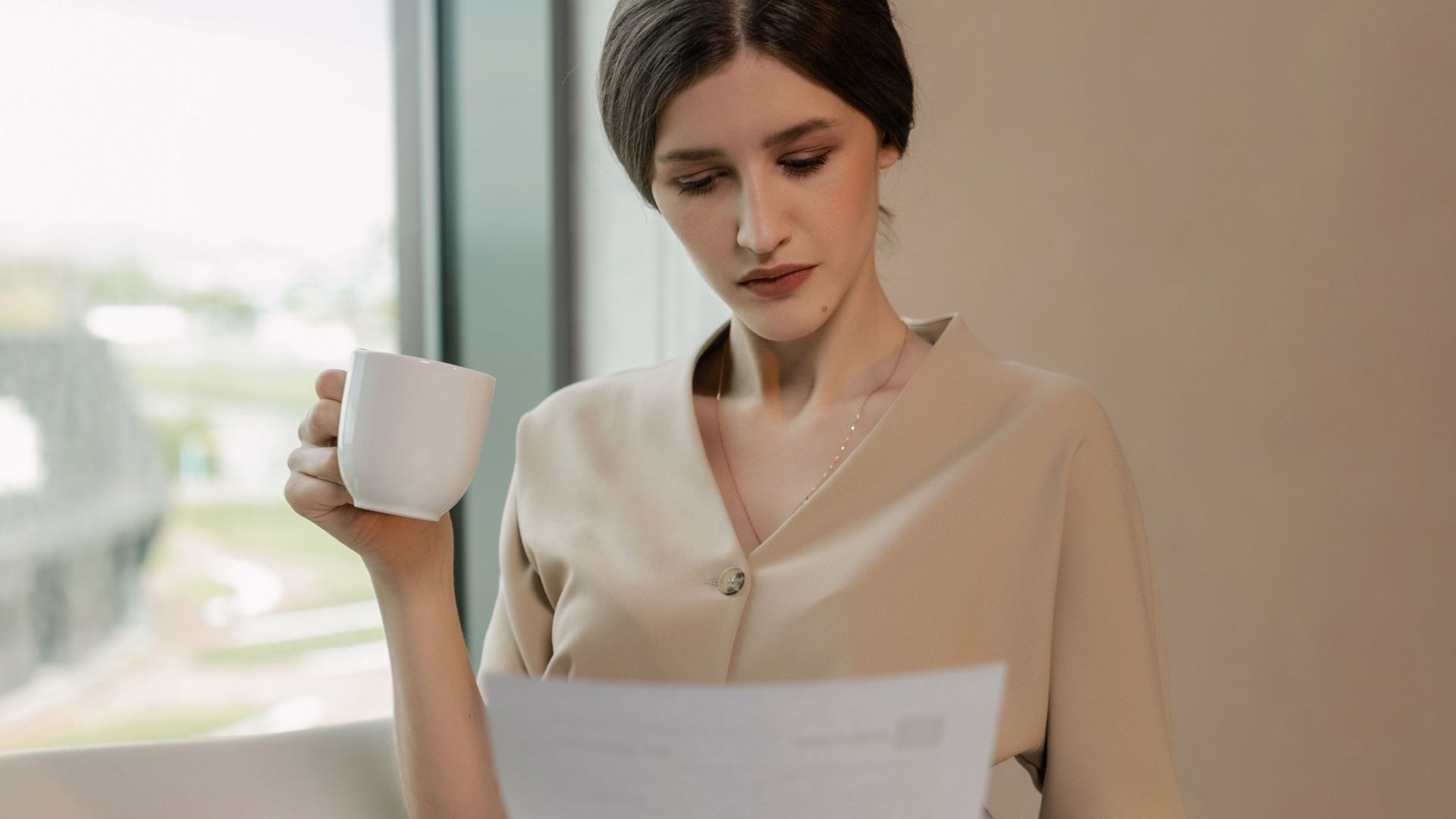 Businesswoman in an office setting reviewing documents while enjoying her coffee.