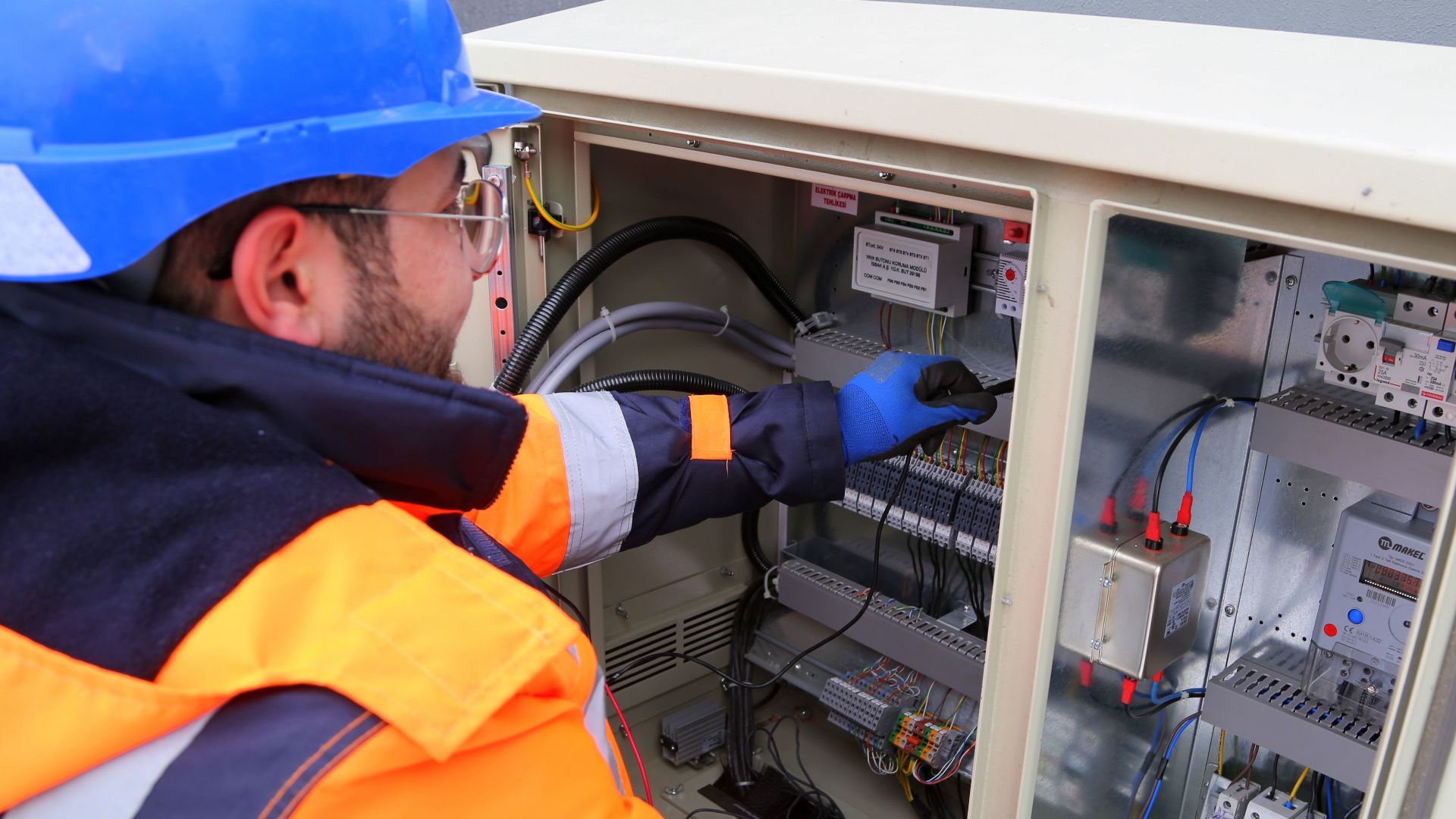 Engineer in safety gear working on an outdoor electrical panel, ensuring system functionality.