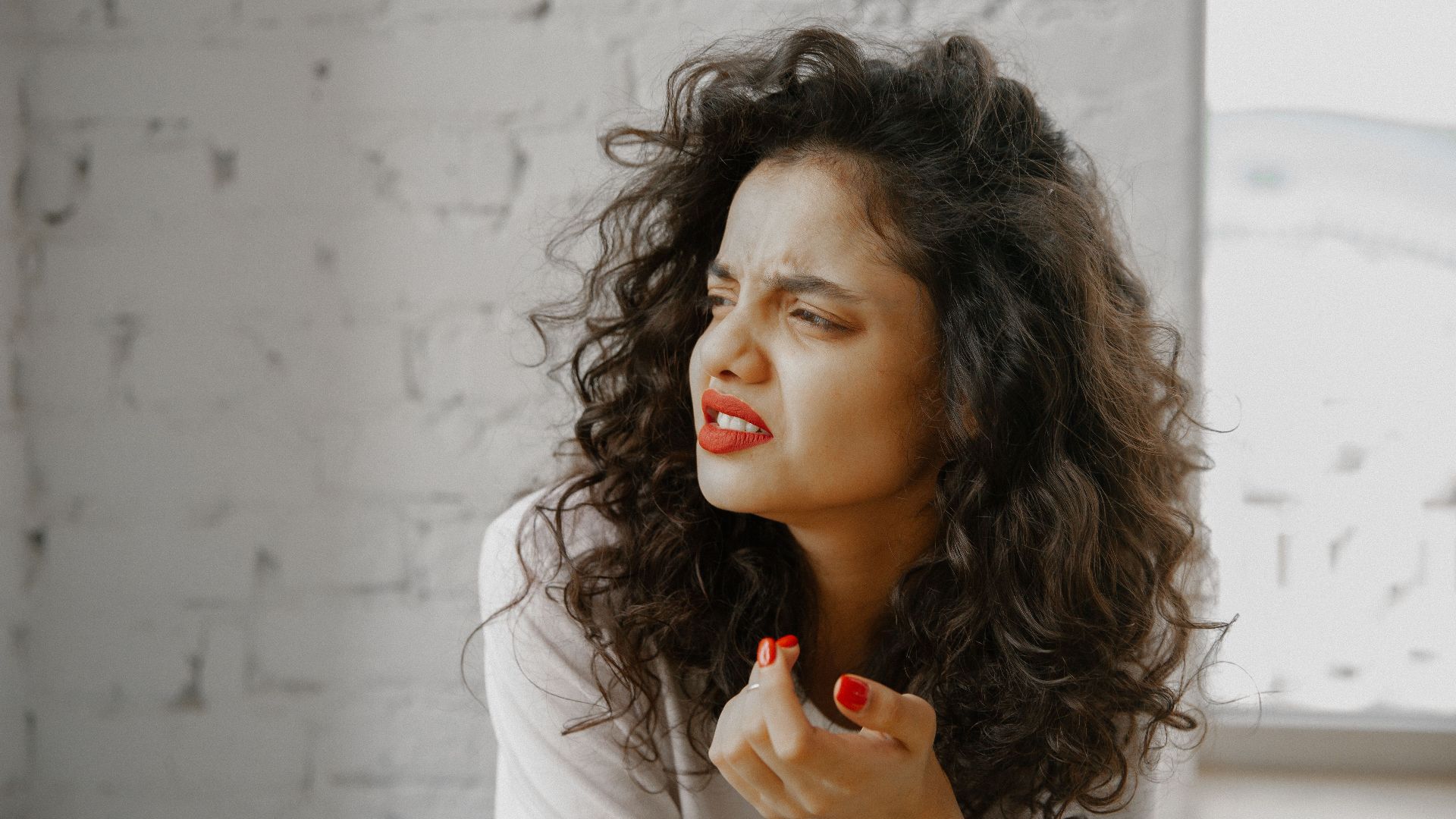 A brunette woman showing an expression of disgust against a brick wall.