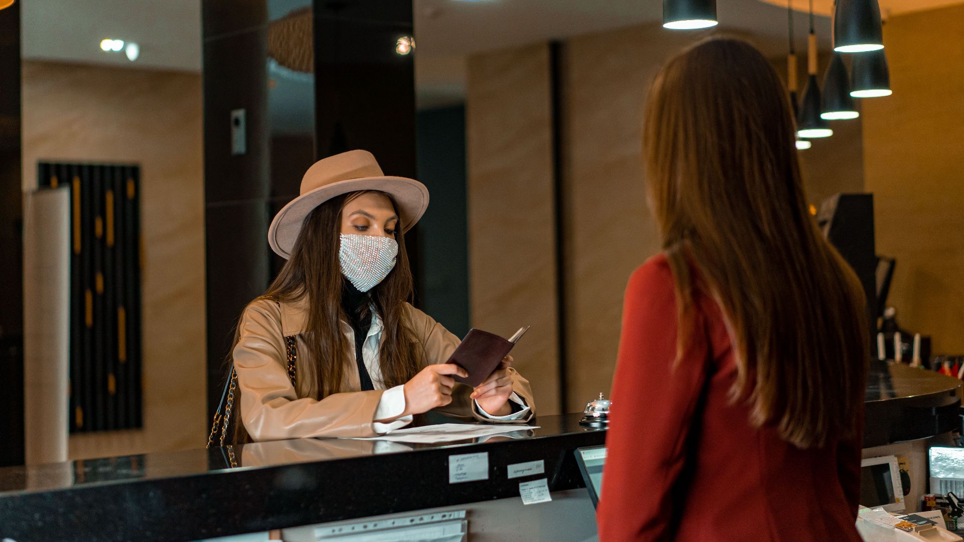 A woman wearing a mask checks in at a hotel reception desk.