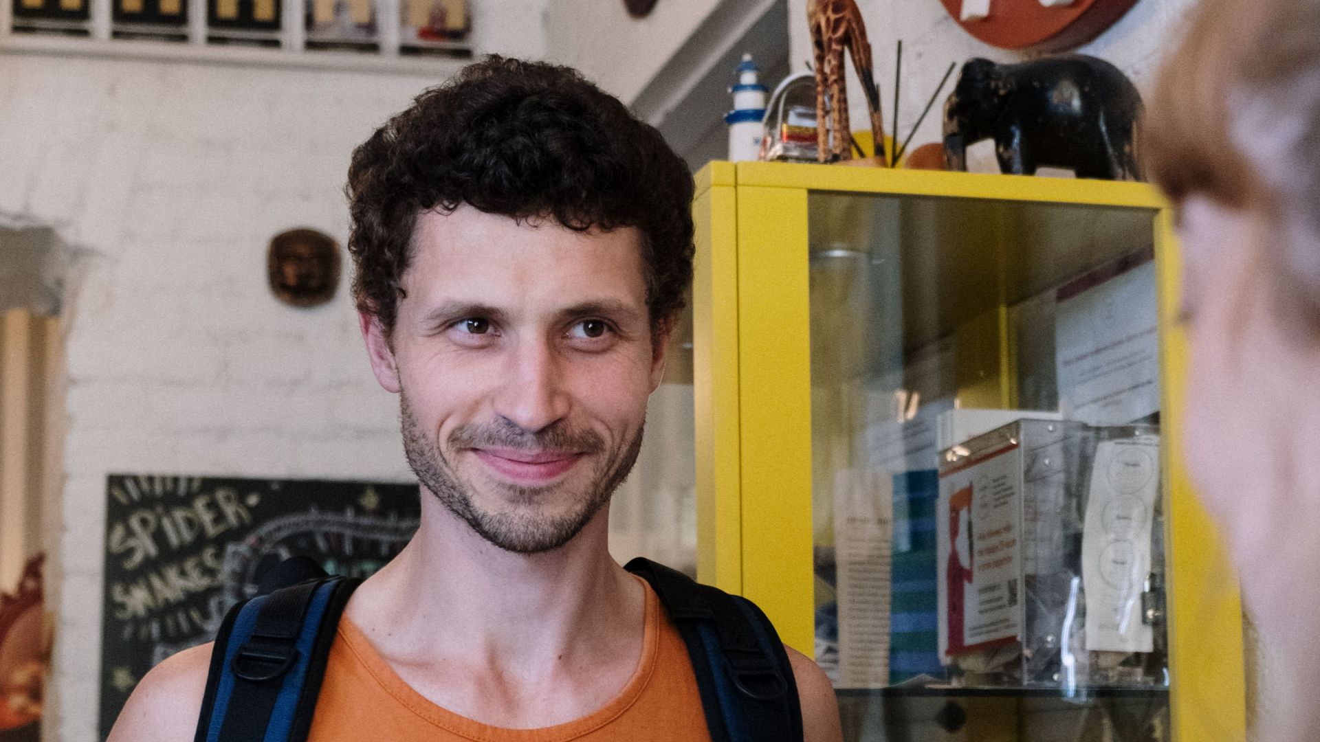 A backpacker checks in at a hostel reception, greeted warmly by a staff member.