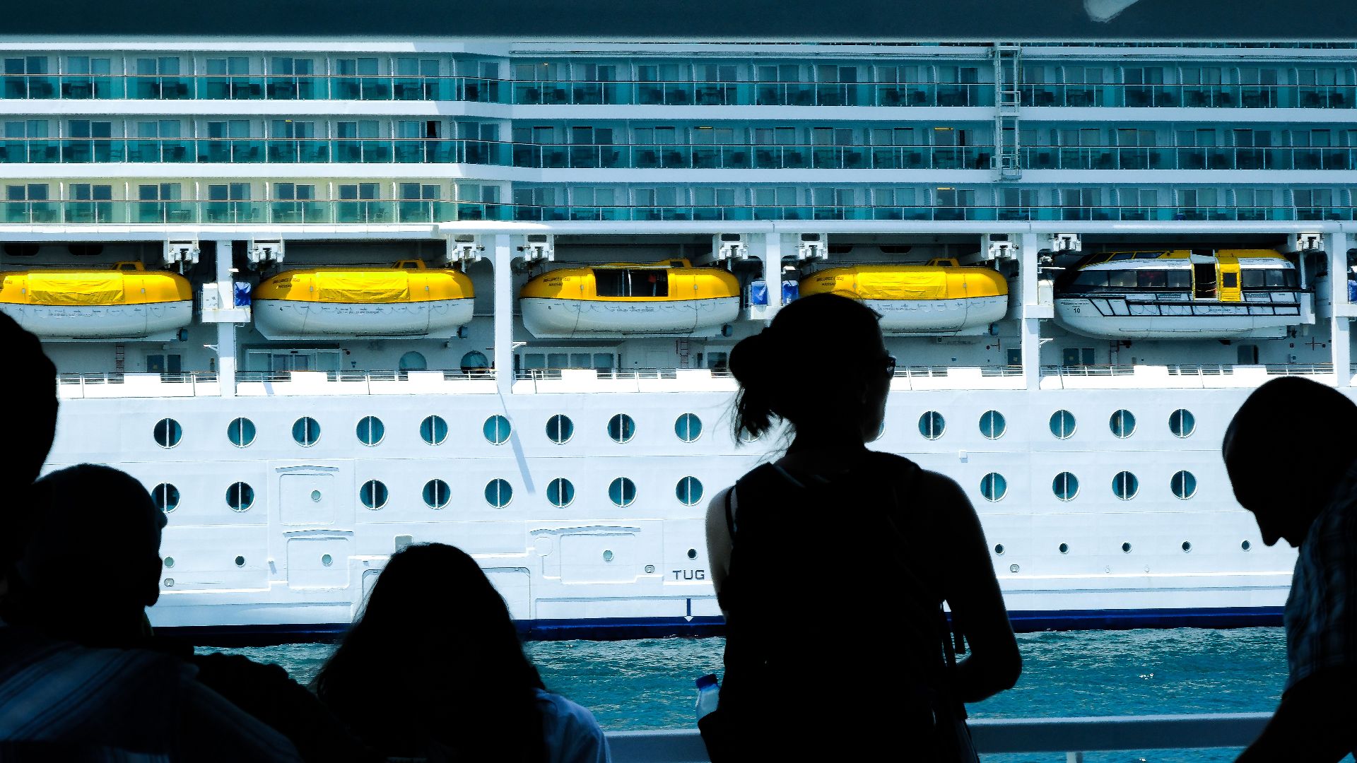 Silhouettes of people observing a large cruise ship from a dock in Türkiye.