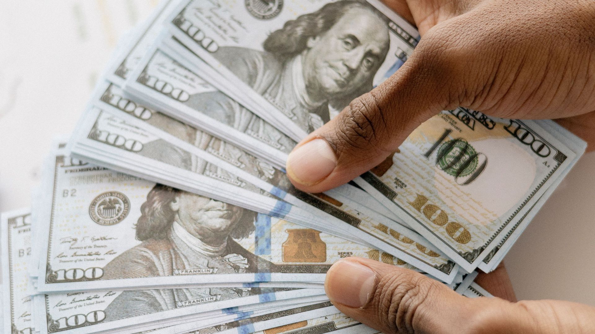 Close-up view of hands counting U.S. hundred dollar bills over a laptop background.