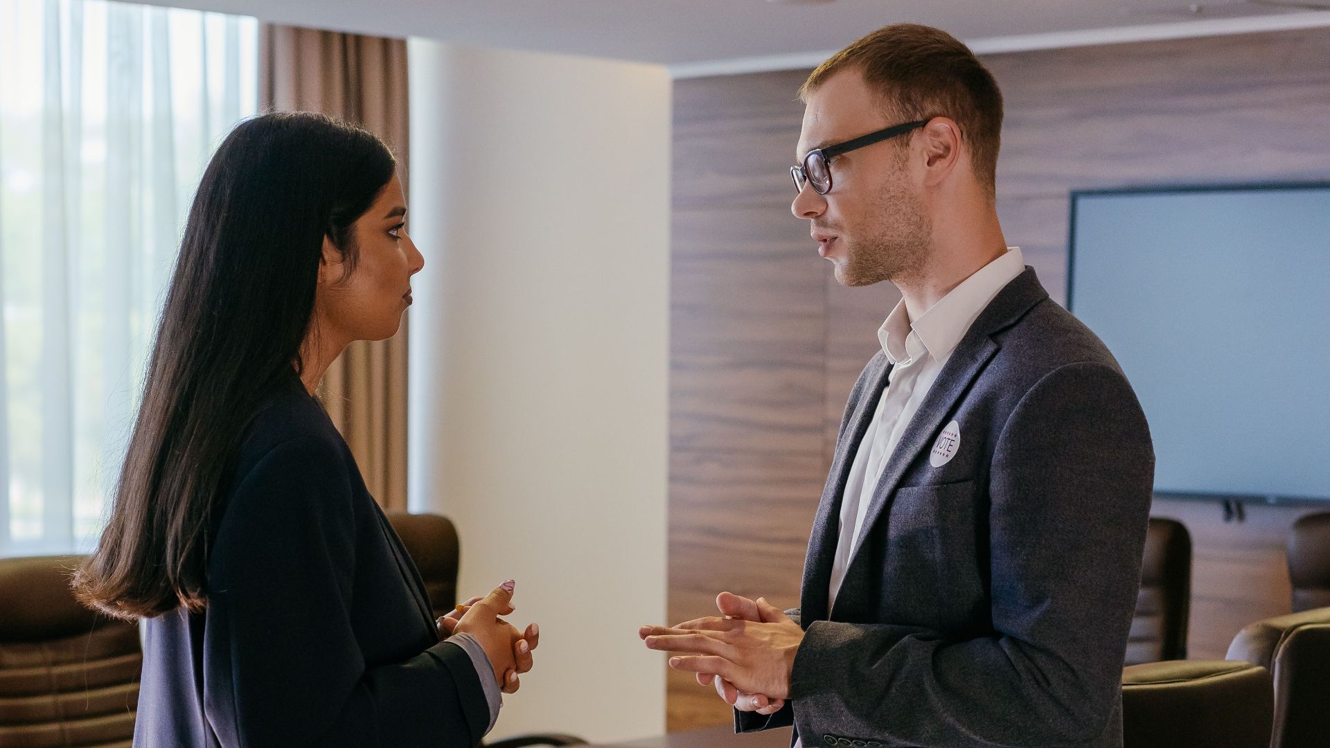 Two professionals engaged in discussion inside a modern conference room setting.