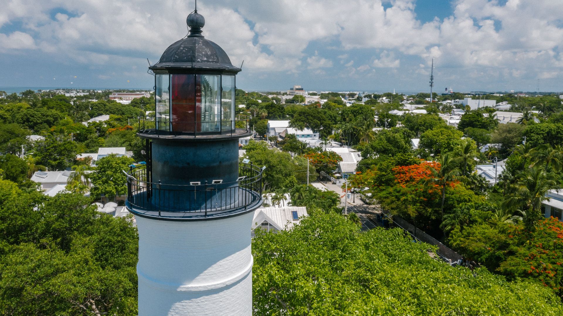 Discover the historic Key West lighthouse surrounded by lush greenery under a bright blue sky.