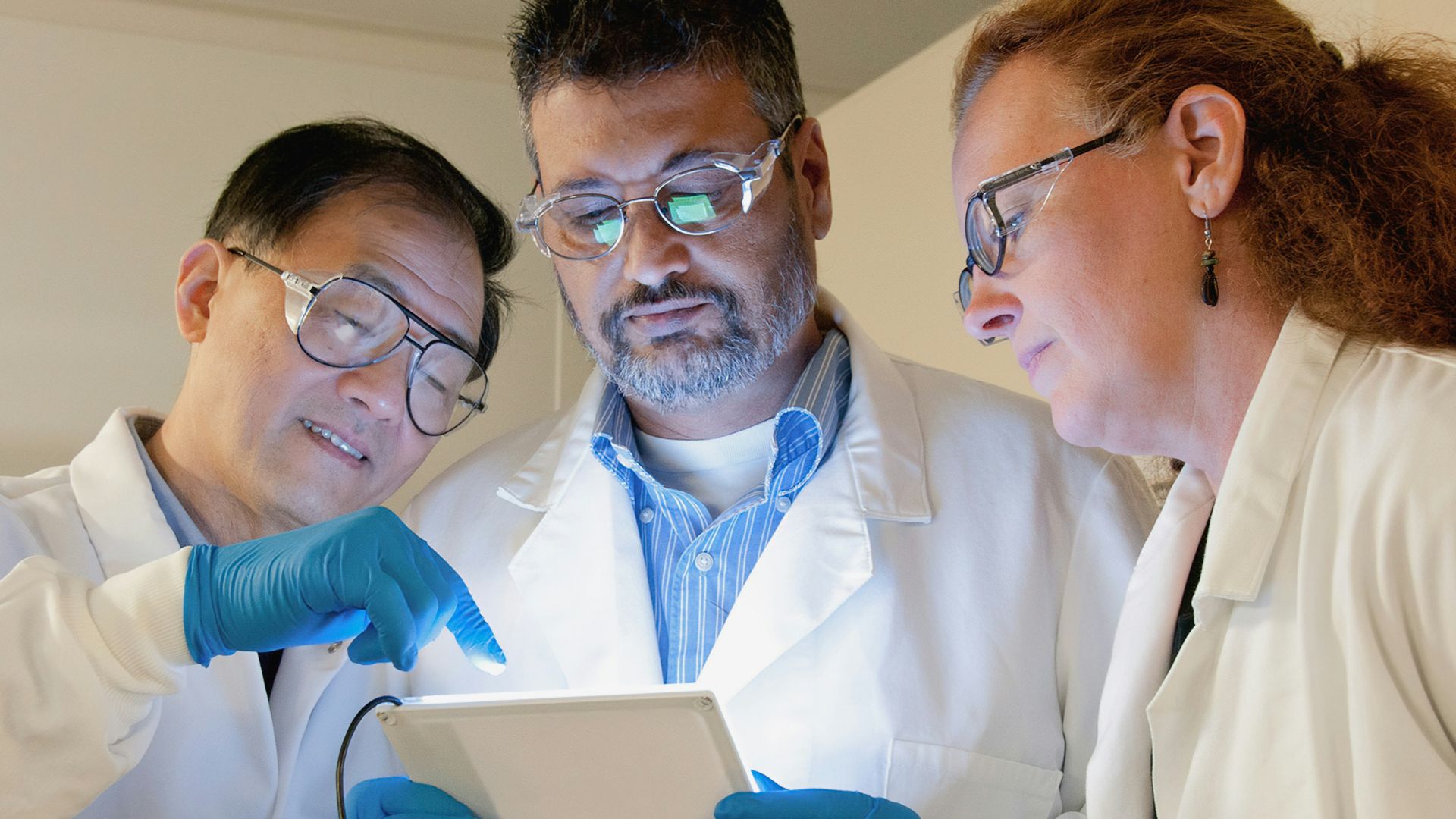 three people in lab coats looking at a tablet