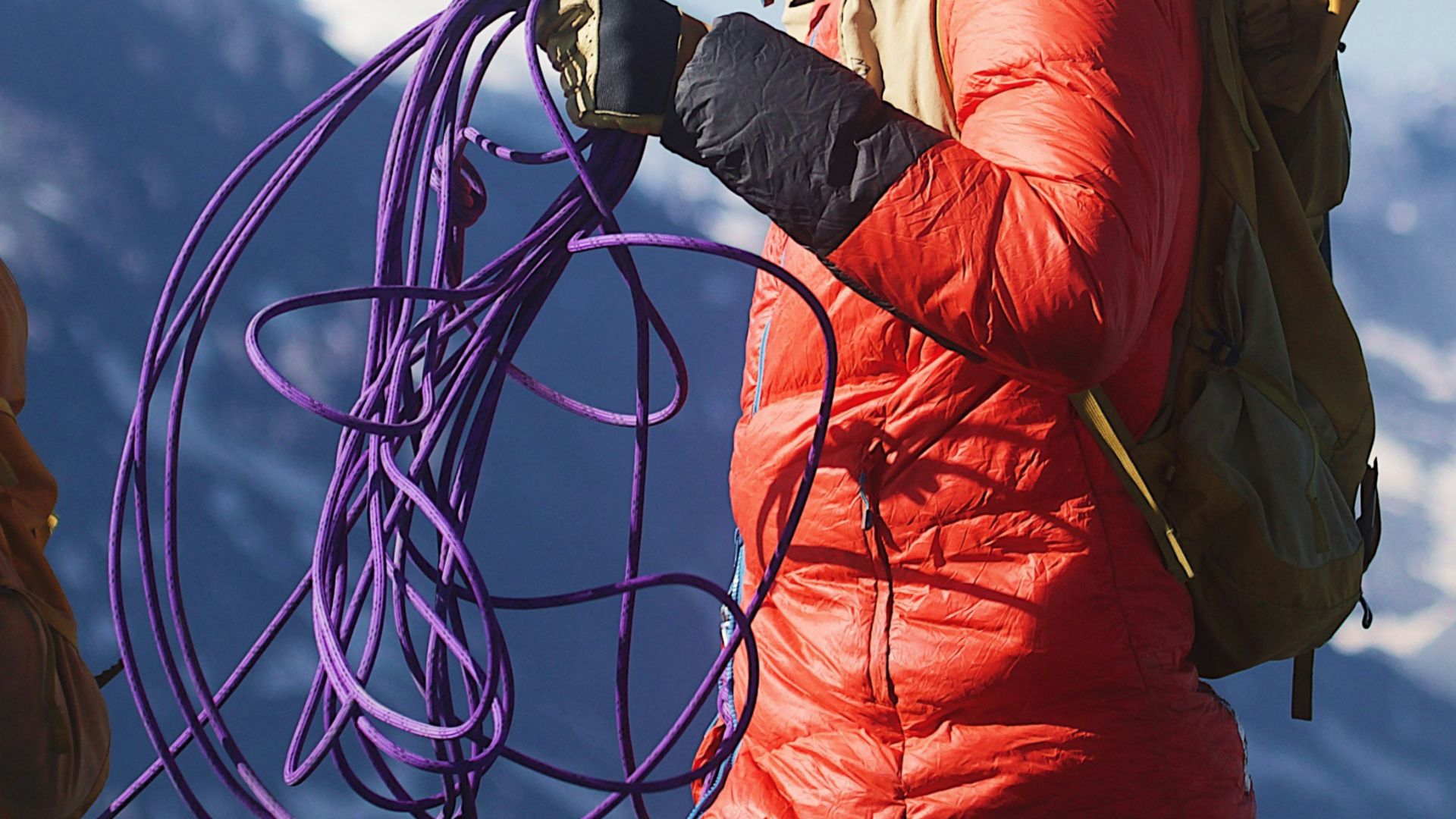A climber in an orange jacket holding a purple rope on a mountain
