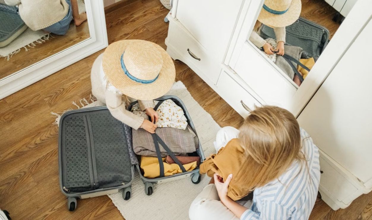 Child packing suitcase with help from mother, preparing for a summer trip.