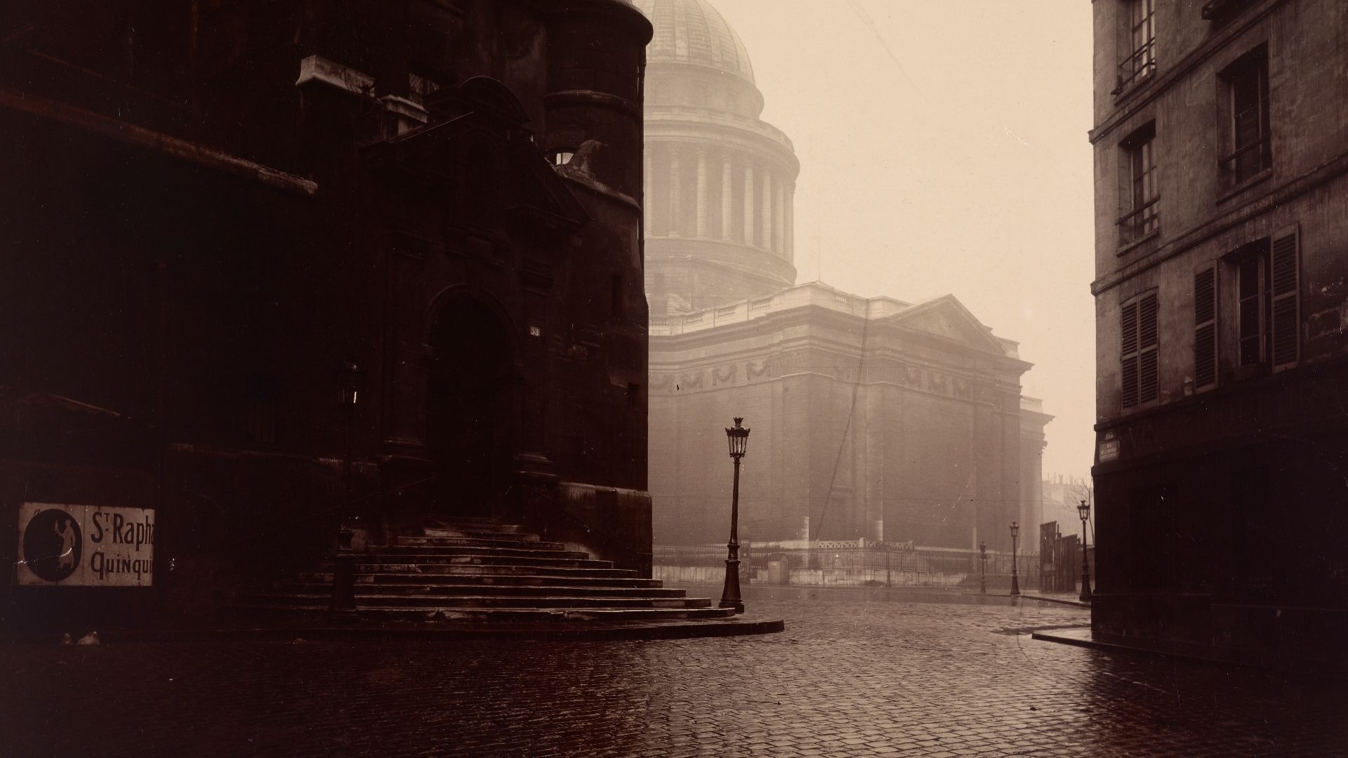 Eugène Atget made this atmospheric study across the place Sainte-Geneviève toward the back of the Panthéon, a church boldly designed to combine the splendor of Greece with the lightness of Gothic churches. The church's powerful colonnaded dome, Atget's pr