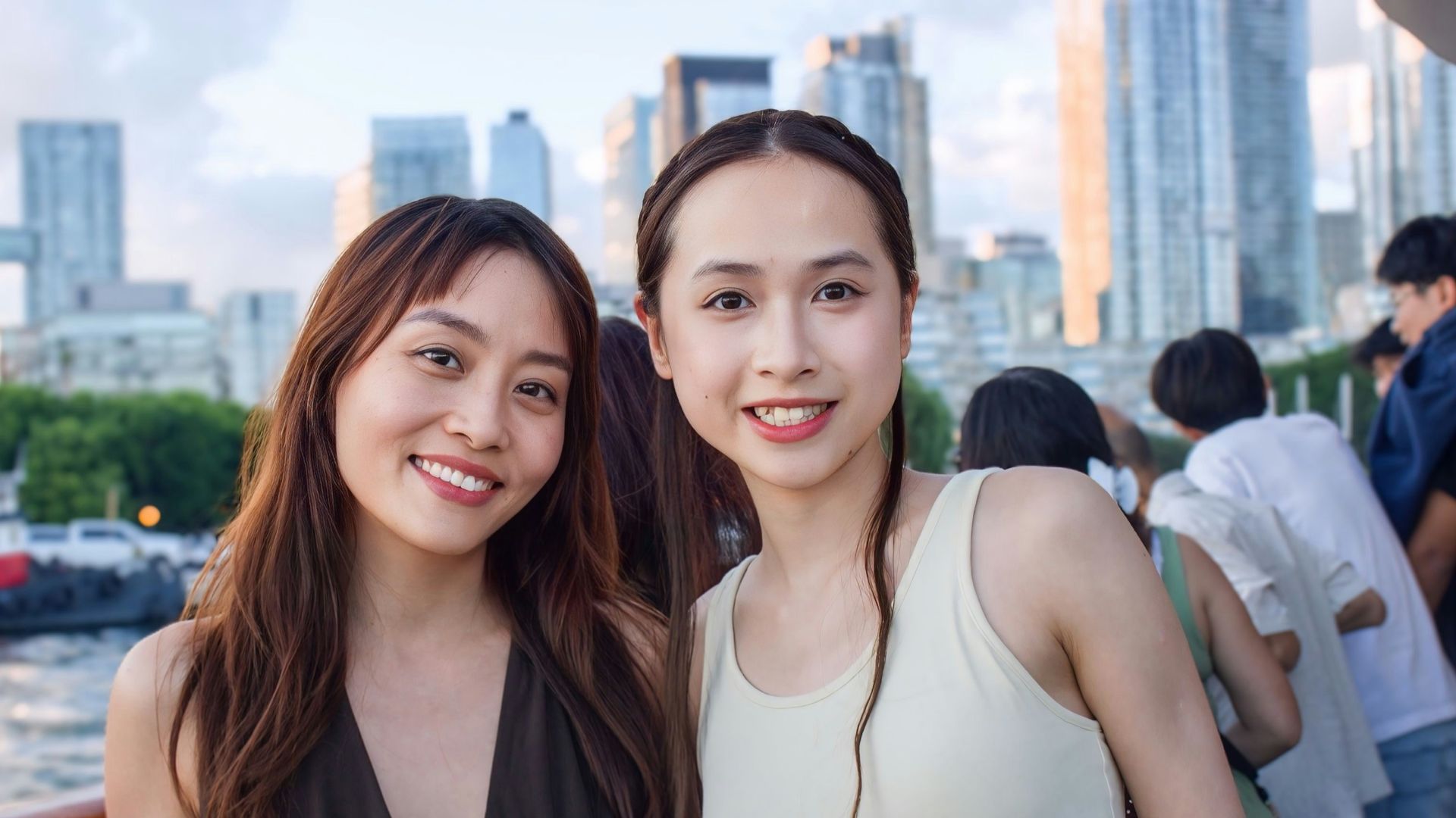 Two women smiling on a boat deck with a city skyline in the background