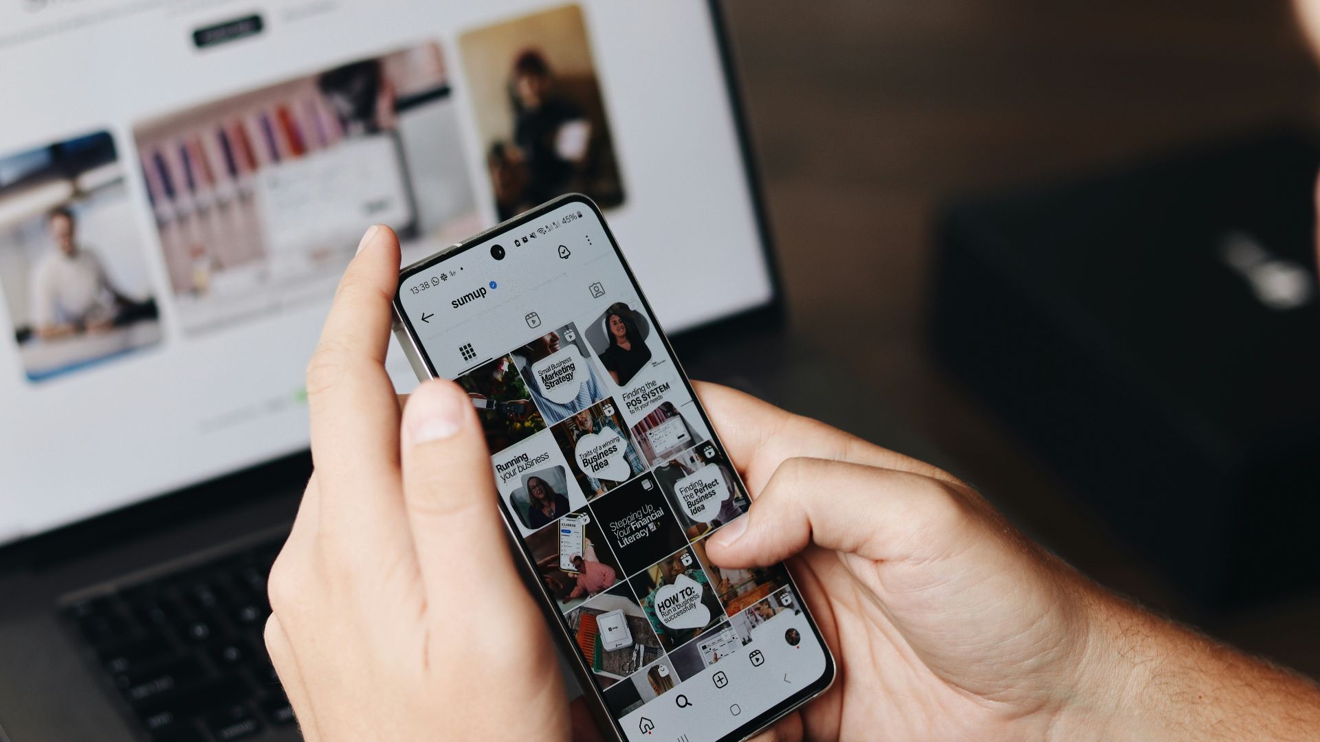 A person holding a cell phone in front of a laptop