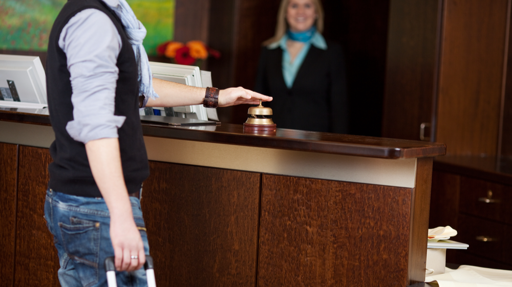 male costumer with baggage ringing bell at hotel front desk