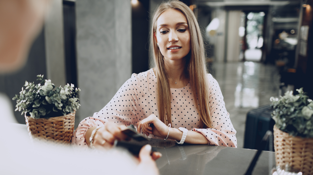 Young beautiful woman hotel guest paying for her stay with credit card at front desk