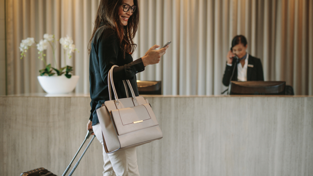 Woman using mobile phone and pulling her suitcase in a hotel lobby