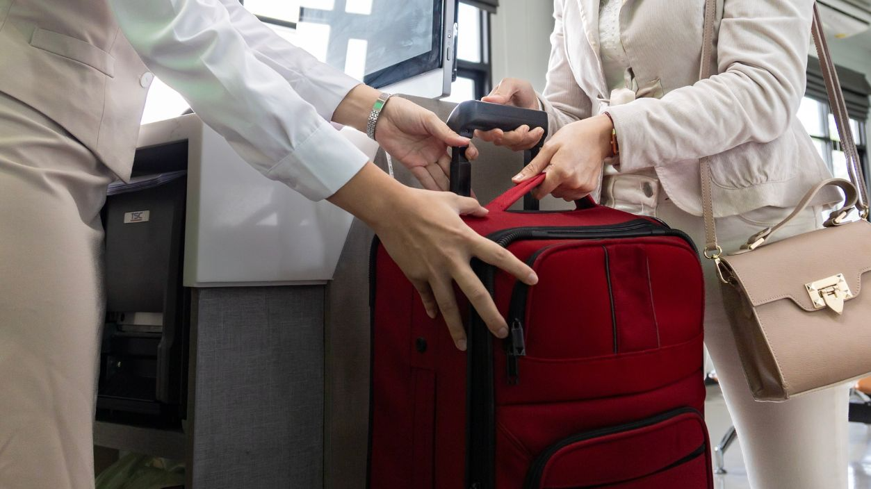 Shutterstock-2465477813, Asian passenger is checking in her big baggage bag to airline ground crew at departure gate into the airplane for measuring weight before boarding into plane