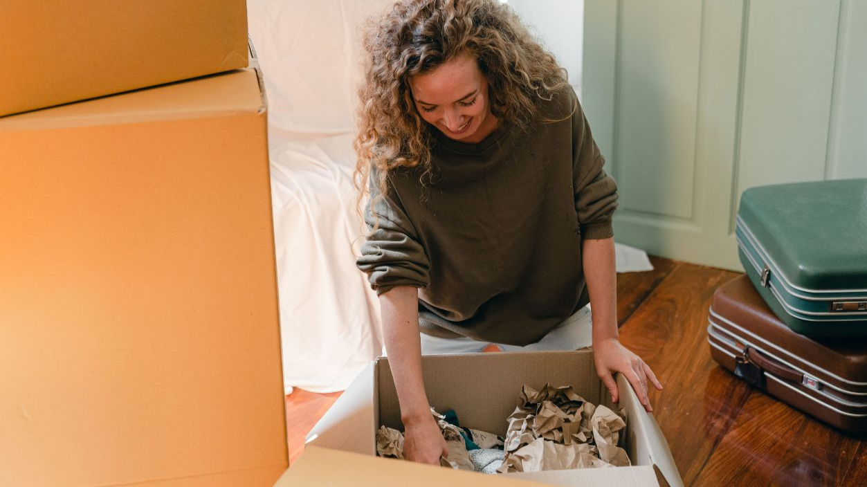 A cheerful young woman unpacking boxes in her new home, feeling content