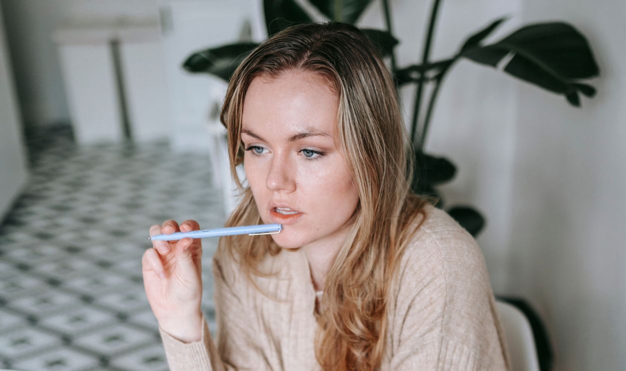 Woman pondering while working at a laptop with books and coffee. Ideal for freelancing