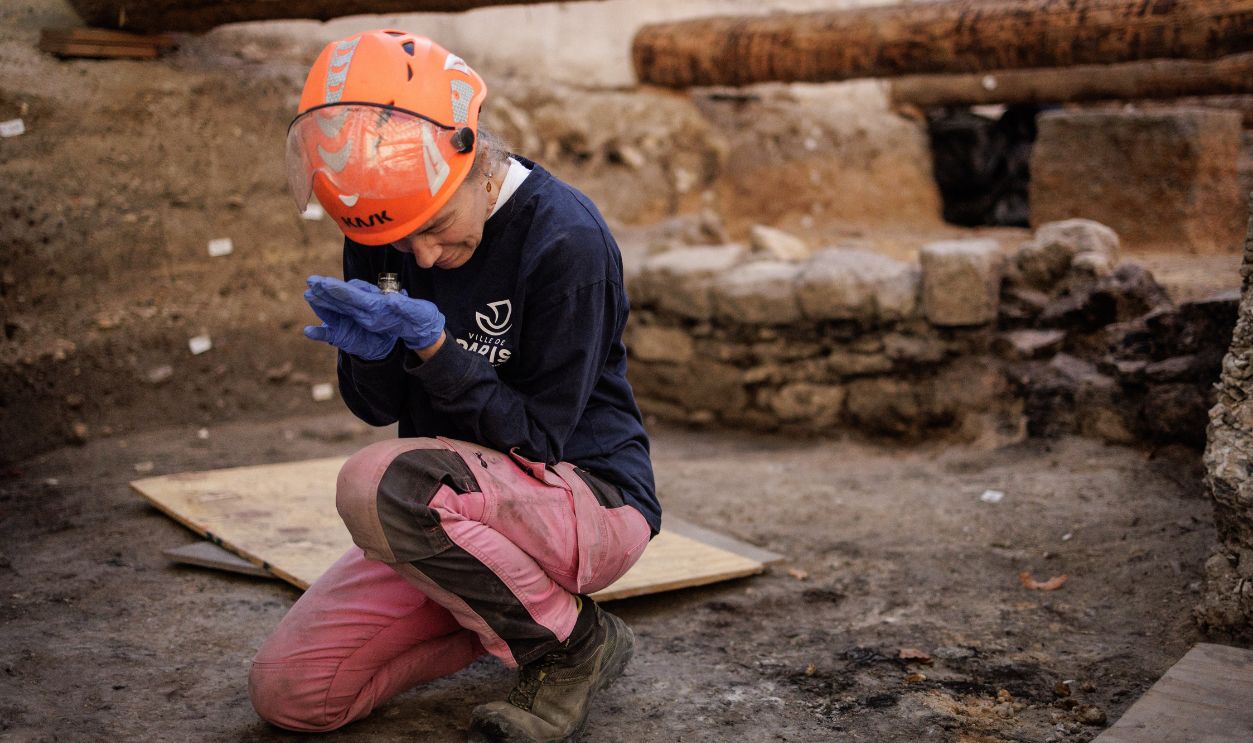 Getty Images - 2296126202 - Elodie Perugini, archeologist for the city of Paris, looks at a Gallic coin using a magnifier during excavations at an archaeological site under the Hotel-Dieu hospital on the Ile de la Cite in central Paris, on September 23, 2026. A Gallo-Roman era wall of Lutetia was recently discovered at the site.