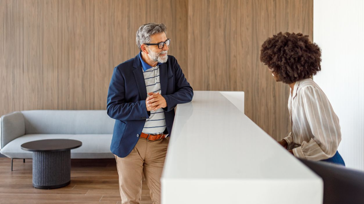 Shutterstock-2738726663, Mature businessman talking with hotel receptionist in lobby regarding room reservation and guest services